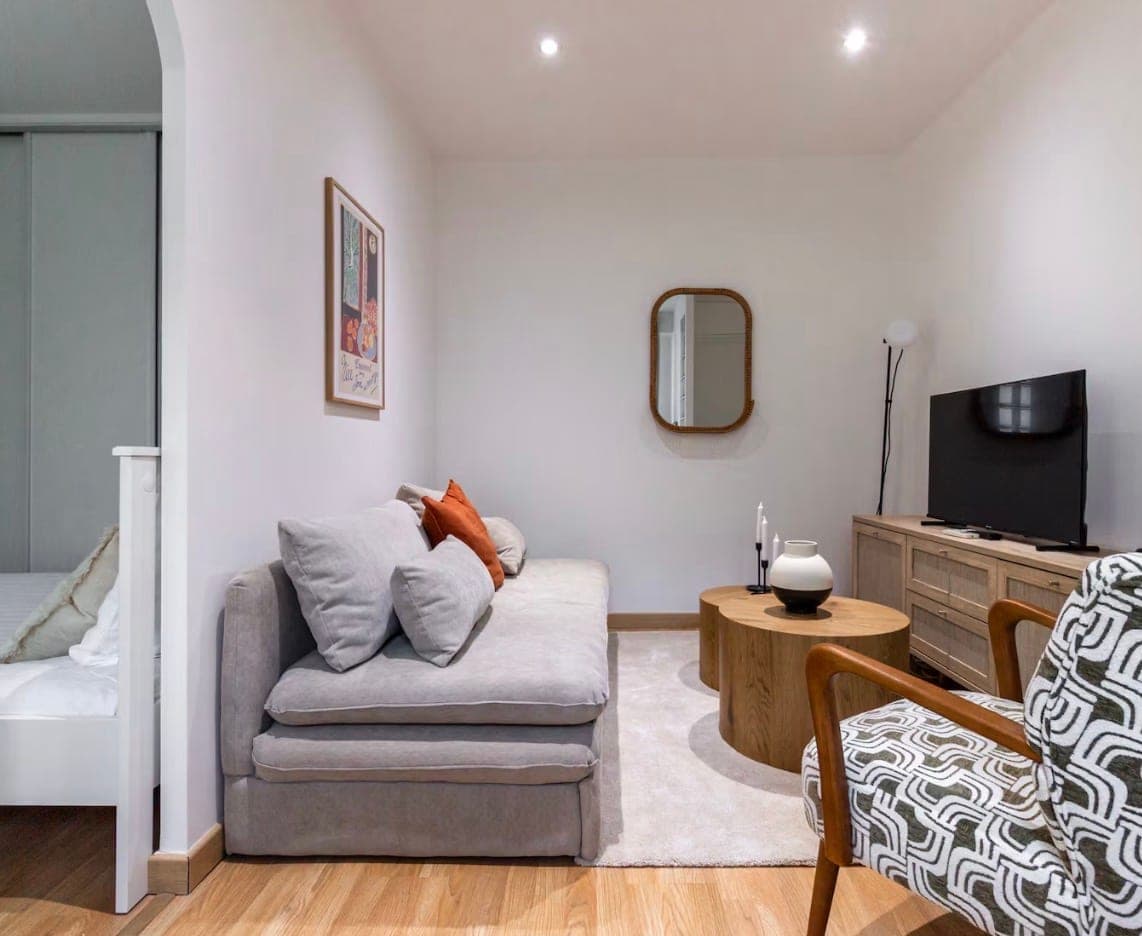 Séjour compact avec canapé gris, meuble télévision et chambre attenante